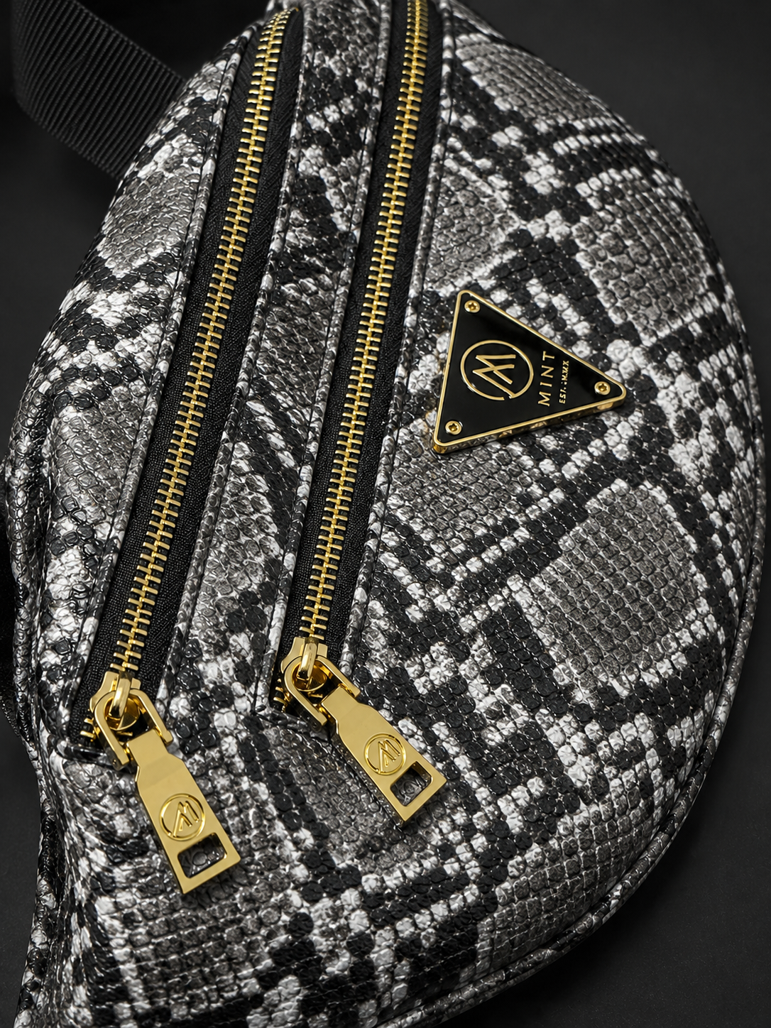 Patterned bag with gold zippers and a brand logo on a dark background