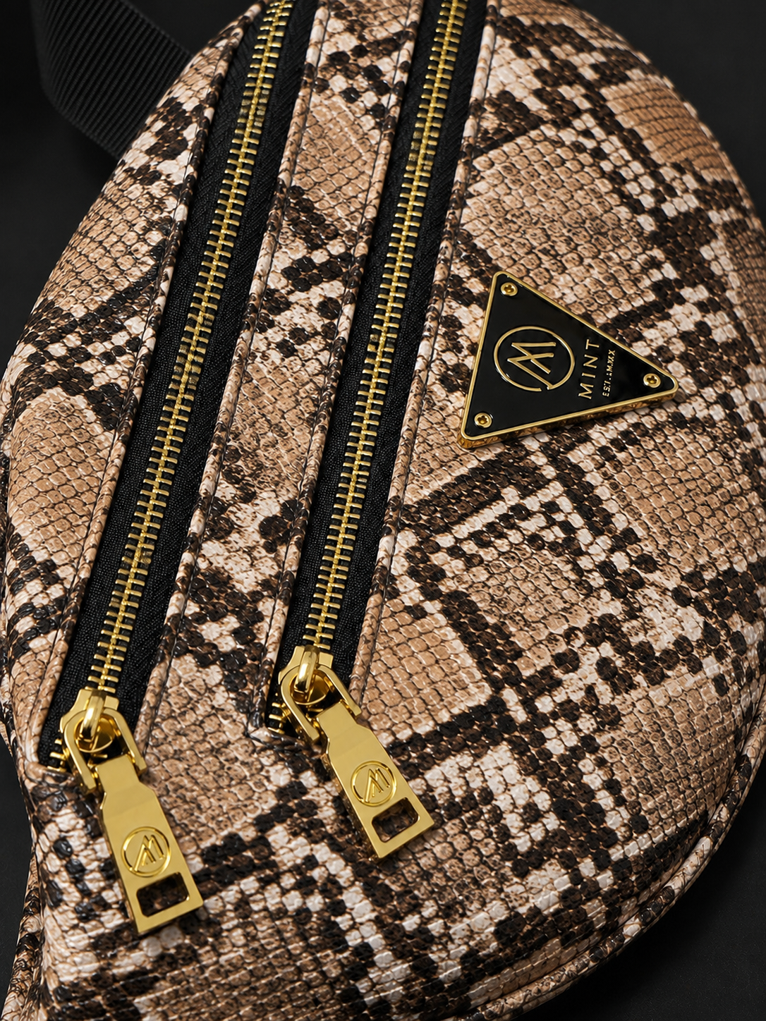 Snakeskin-patterned bag with gold zippers and a brand logo on a dark background